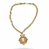 Collar de cadena de eslabones gruesos en acero dorado, con un dije central de diseño circular tipo moneda antigua con textura rugosa y una piedra rectangular clara engastada en el centro.