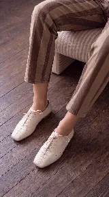 Zapato acordonado tipo oxford de cuero color off-white, con punta cuadrada, costuras decorativas y cordones finos al tono.
