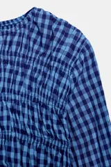 Camisa de manga larga con cuello redondo, confeccionada en tejido de cuadros vichy en tonos de azul. Presenta un fruncido elástico en el torso y puños con elástico.