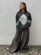Sweater de punto con diseño de rombos en tonos gris oscuro y gris claro, de corte holgado, cuello redondo y manga larga.