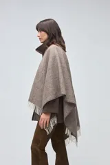 Ruana de lana sin teñir en tonos beige, con textura acanalada y terminaciones con flecos en los bordes.