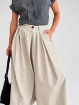 Pantalón palazzo color beige, de tiro alto y calce amplio, con pinzas frontales y bolsillos laterales.