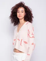 Cardigan corto de tejido de punto color crema con diseño de caras abstractas en azul, escote en V, manga larga y tres botones de plástico.