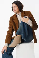 Bota de cuero color beige con diseño versátil que incluye una polaina desmontable, permitiendo transformar su silueta. Presenta punta fina, taco bajo y un detalle de logo bordado en el lateral.