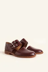 Zapato tipo oxford abierto en los laterales, confeccionado en cuero vacuno negro. Presenta doble tira con hebillas metálicas en el empeine y detalle de tachas plateadas en el contorno del talón y la puntera.