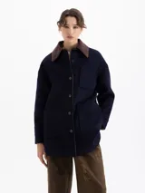 Chaqueta reversible de corte recto. Un lado confeccionado en paño azul marino con cuello de corderoy color chocolate, bolsillos frontales y cierre de botones. El lado interno está realizado en nylon color verde militar.