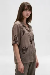 Camisa de algodón con estampado en tonos claros sobre base azul oscura, cuello solapa, mangas cortas y cierre frontal con botones.