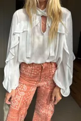 Blusa de gasa blanca con sutil estampado dorado, diseño con volados en las mangas y lazo en el cuello. Presenta una leve transparencia y caída fluida.