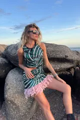 Conjunto de dos piezas compuesto por un top sin mangas y una falda corta, ambos confeccionados en tela de lentejuelas con diseño de rayas diagonales en tonos verde y plateado. La falda presenta un borde inferior decorado con plumas rosadas.