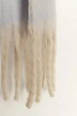 Bufanda manta de tejido suave y peluche, color celeste claro, con flecos largos en los extremos de color beige.