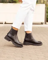 Botinetas tipo Chelsea de cuero negro, con paneles laterales elásticos y suela track dentada de goma. Presentan una combinación de texturas entre cuero mate y cuero charolado en la puntera y el talón.