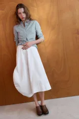 Falda midi de tiro medio en color blanco, con diseño asimétrico en el bajo y bolsillos delanteros. Cuenta con cierre lateral oculto.