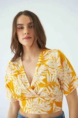 Blusa estampada con diseño de hojas en color amarillo y blanco, con escote en V cruzado, mangas cortas y elástico en la cintura.