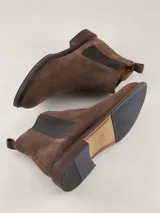 Bota Chelsea de gamuza gris con elásticos laterales, suela de goma marrón y tirador trasero.