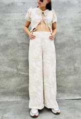 Pantalón palazzo color beige con estampado de flores blancas, cintura alta con elástico y corte amplio.