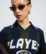 Buzo de punto con diseño de rayas verticales en azul marino y verde, cuello tipo polo y estampado frontal con la inscripción 'PLAYER CLUB'. Presenta un corte regular y mangas largas.