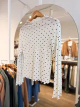 Remera de tul de manga larga con estampado de lunares negros sobre fondo blanco. Presenta cuello y bordes con terminación ondulada.