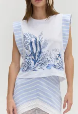 Remera blanca sin mangas con bordado y estampado de corales en tonos azules, con hombreras estructuradas decoradas con rayas celestes y blancas.