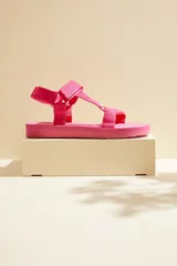 Sandalias planas color fucsia, con tiras de tela ajustable mediante cierre de velcro y suela de plataforma baja.