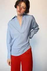 Camisa de manga larga en color celeste con estampado de rayas finas, cuello solapa y escote en pico con detalle de solapa frontal. Presenta puños abotonados y bajo asimétrico.