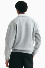 Buzo gris melange con cuello polo y solapa blanca, manga larga, hombros caídos y una franja horizontal blanca en el pecho.