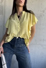Camisa amarilla de mangas cortas con volados, cuello mao y botones frontales.