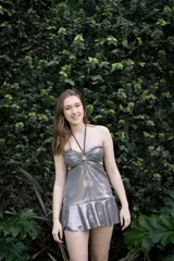 Vestido corto de lentejuelas color ciruela o morado oscuro, con escote corazón y detalle de argolla central que conecta con tirantes finos que atan al cuello. Presenta aberturas laterales (cut-outs) en la zona de la cintura y falda corta con vuelo.