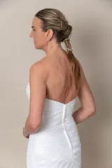 Vestido de novia blanco, sin mangas, con escote corazón y espalda en V. Confeccionado en tafeta drapeada con bordados blancos. Falda con volados y tajo frontal.