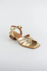 Sandalias doradas con capellada de cuero metalizado y malla, puntera cuadrada, tira ajustable al tobillo y taco geométrico de madera.