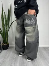Pantalón baggy gris con efecto lavado, bolsillos traseros con bordado de llamas blancas y corte holgado.