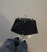 Short de cuero sintético negro con cierre frontal de botón y bolsillos decorativos tipo ojal.