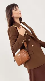 Bandolera de diseño acolchado con costuras geométricas, color verde oliva. Cuenta con doble compartimento con cierre metálico, placa metálica con logo en el frente y correa de cinta ajustable y extraíble.