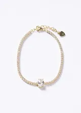 Pulsera tipo tennis de plata 925 con baño de oro 18k, compuesta por una hilera de pequeñas zirconias brillantes y una zirconia central de corte ovalado. Incluye cierre de mosquetón y cadena de extensión con dije en forma de corazón.