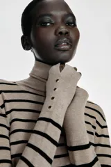 Jersey de punto liso en color beige, con cuello alto y manga larga con detalle de botones metálicos en los puños.
