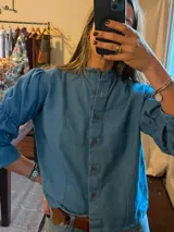 Camisa de denim azul con cuello mao, cierre frontal con botones y mangas largas con frunces.