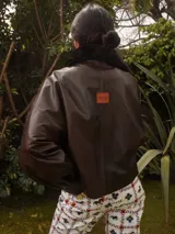 Campera oversize de cuero tostado con solapas y forro interno de corderito sintético azul marino, mangas anchas y detalles de costuras trenzadas.