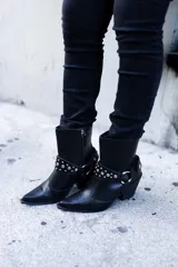 Bota texana corta de cuero negro con textura de piel de serpiente, punta fina y taco cubano. Presenta arnés desmontable con apliques metálicos plateados.