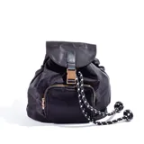 Mochila negra de tela impermeable con bolsillo frontal con cierre dorado, solapa con hebilla metálica dorada y cordón ajustable.