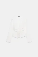 Top de manga larga con textura nido de abeja, escote en pico con detalle de volantes y cierre frontal mediante lazos ajustables.