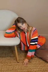 Sweater de algodón tejido a rayas verticales en el cuerpo y horizontales en las mangas. Presenta una mezcla de colores vibrantes como naranja, rosa, verde azulado, marrón, blanco, negro y violeta. Tiene terminaciones en crochet en los puños.