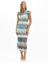 Vestido midi confeccionado en tejido de punto calado, con patrón geométrico en zigzag en tonos blanco, marrón, tostado y azul. Presenta escote a la base, mangas cortas con volados en los hombros, silueta recta y forro interior a tono. Incluye un cinturón fino con hebilla metálica.