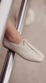 Zapato de cuero marrón chocolate con cordones finos negros, punta cuadrada y detalles de perforaciones decorativas en los laterales.