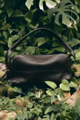 Bolso de hombro de formato alargado confeccionado en piel con textura granulada. Presenta un diseño con pespuntes decorativos en el cuerpo, asa fija para llevar al hombro y cierre mediante cremallera. Incluye un bolsillo interior extraíble.
