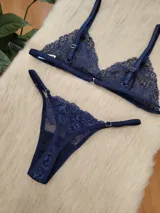 Conjunto de lencería de encaje en color azul profundo, compuesto por un corpiño triangular sin aro y una bombacha tipo colaless con detalles de encaje y transparencias.