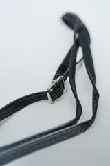 Cartera negra de cuero sintético con tachas metálicas plateadas en los bordes y cierre superior. Incluye correa larga ajustable.