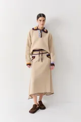 Falda midi de lana con diseño acampanado y textura acanalada. Presenta una cintura elástica con cordón ajustable, bolsillos laterales con detalles en contraste de colores y un borde inferior con costura decorativa visible.