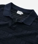 Remera tipo polo de manga corta con cuello en V, confeccionada en un tejido con textura patchwork. Presenta un diseño elegante y versátil, ideal para un look casual o formal.