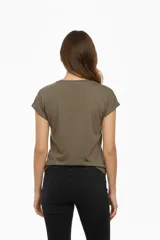 Remera de algodón color verde militar, manga corta con puños doblados y cuello redondo. Presenta un estampado frontal con motivos florales y un fondo con patrón de cuadros en tonos rosados, marrones y verdes.