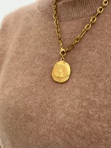 Collar de cadena de eslabones gruesos con dije de medalla ovalada con relieve de la Virgen, acabado en tono dorado con textura artesanal.