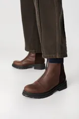 Bota corta de cuero color marrón con cierre frontal, suela track negra y paneles laterales en gamuza de un tono más oscuro.